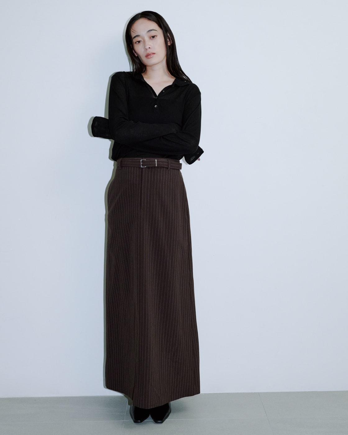 黒いシャツにブラウンのロングスカートを着た女性が正面を向いている画像