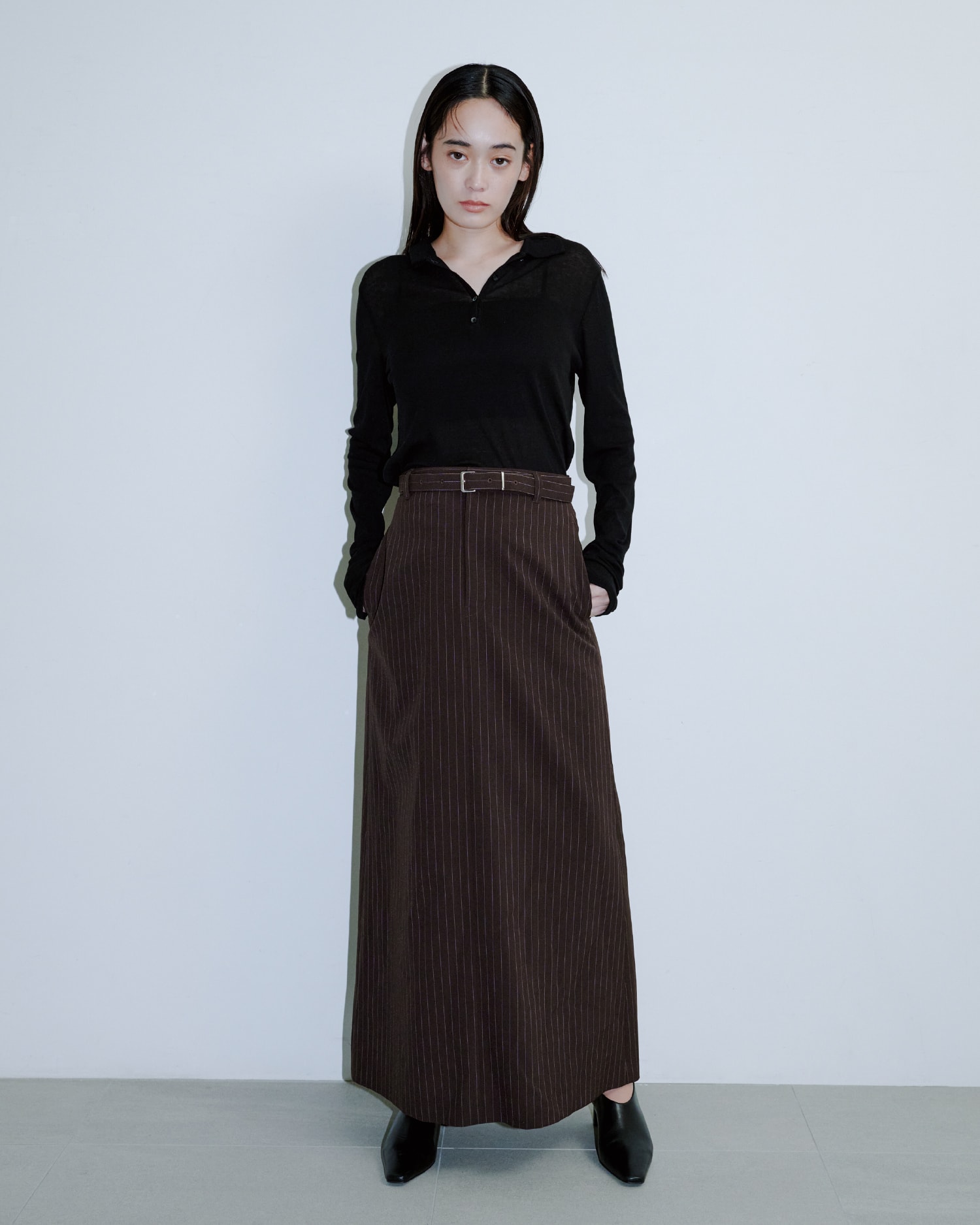黒いシャツにブラウンのロングスカートを着た女性が正面を向いている画像