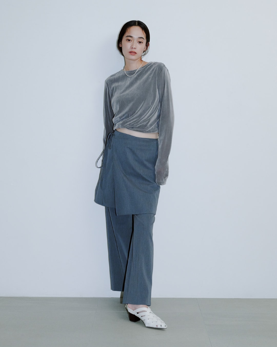 グレーのトップスにブルーのパンツを着た女性が正面を向いている画像