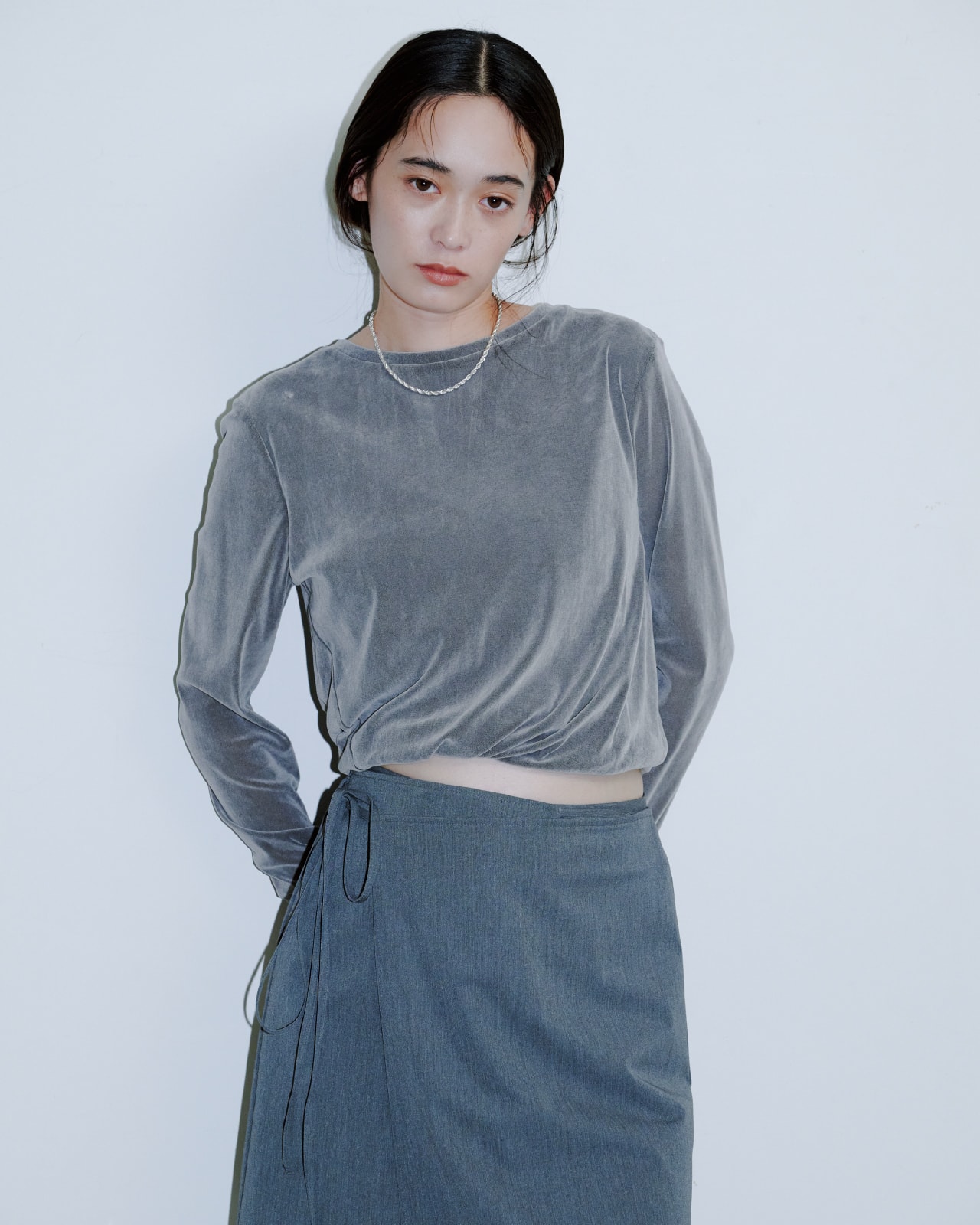 グレーのトップスにブルーのパンツを着た女性が正面を向いている画像