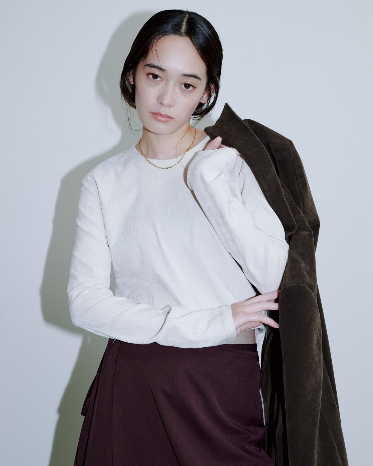ブラウントップスに白シャツとブラウンのパンツを着た女性が正面を向いている画像