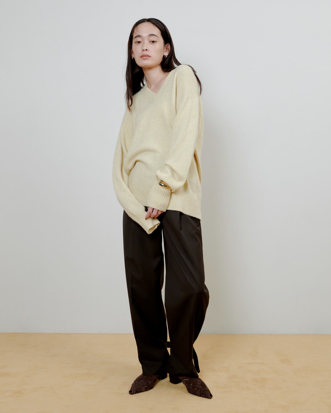 黄色いニットに黒いパンツを着た女性が正面を向いている画像