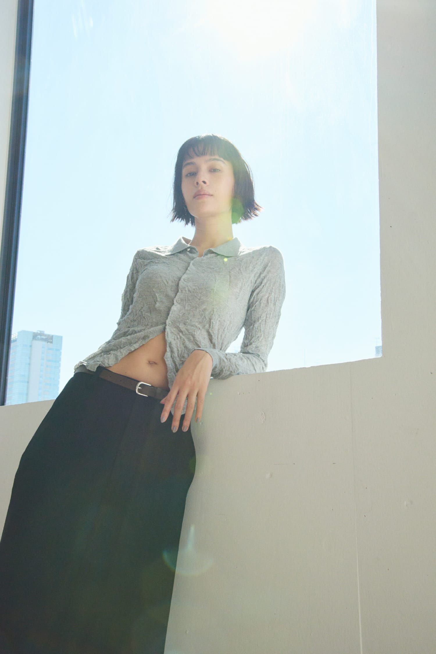 ワッシャーニットシャツ&からみ織りセミフレアスカート&レザートングストラップサンダル&レザーベルトを着用した女性