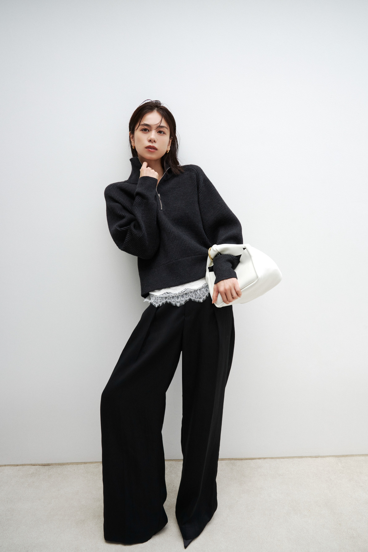チャコールのニットと黒のパンツに白のバッグを持つ佐藤晴美（look 03 1枚目）