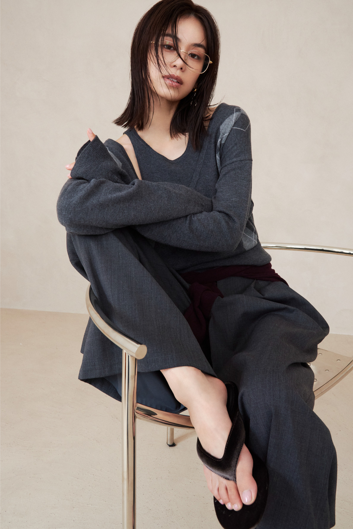 グレーのニットと黒のパンツで椅子に腰掛ける佐藤晴美（look 04 1枚目）