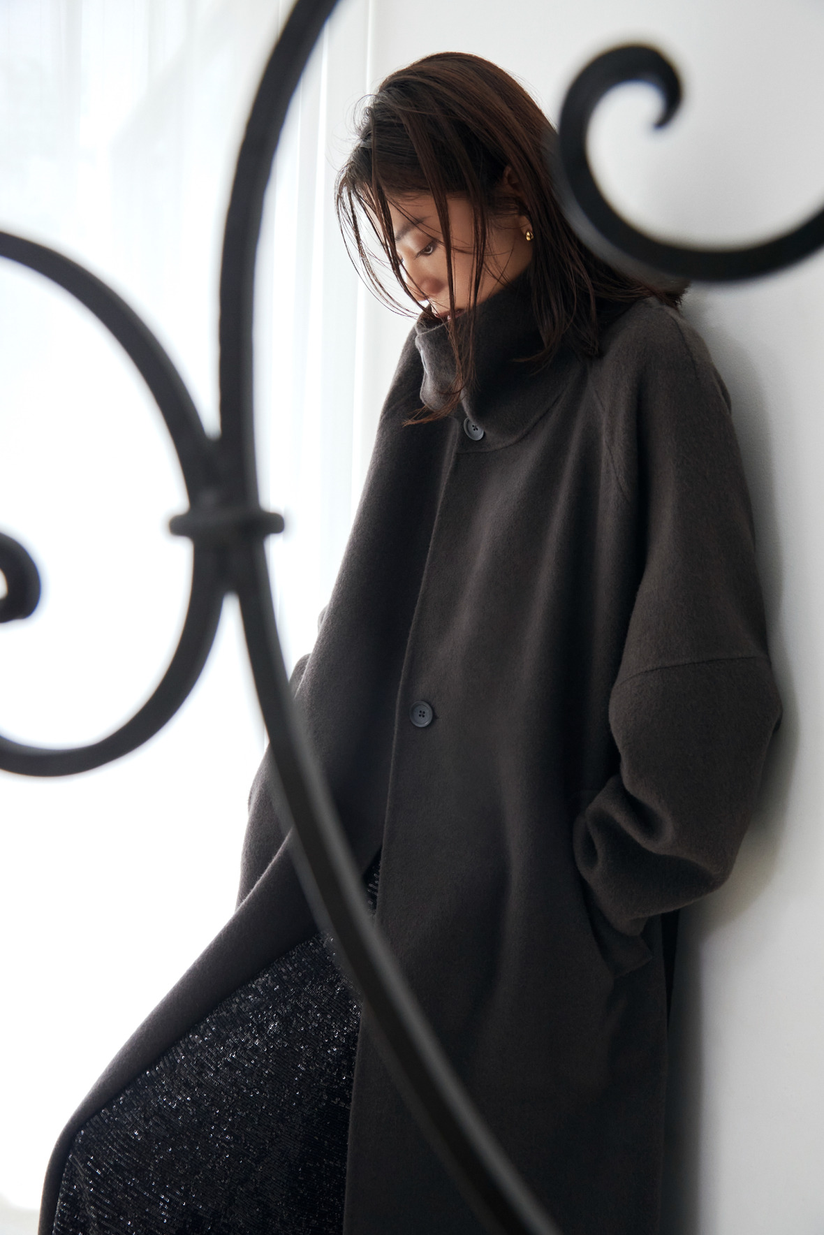 Look04 黒のロングコートで鉄細工の前に立つ着用カット